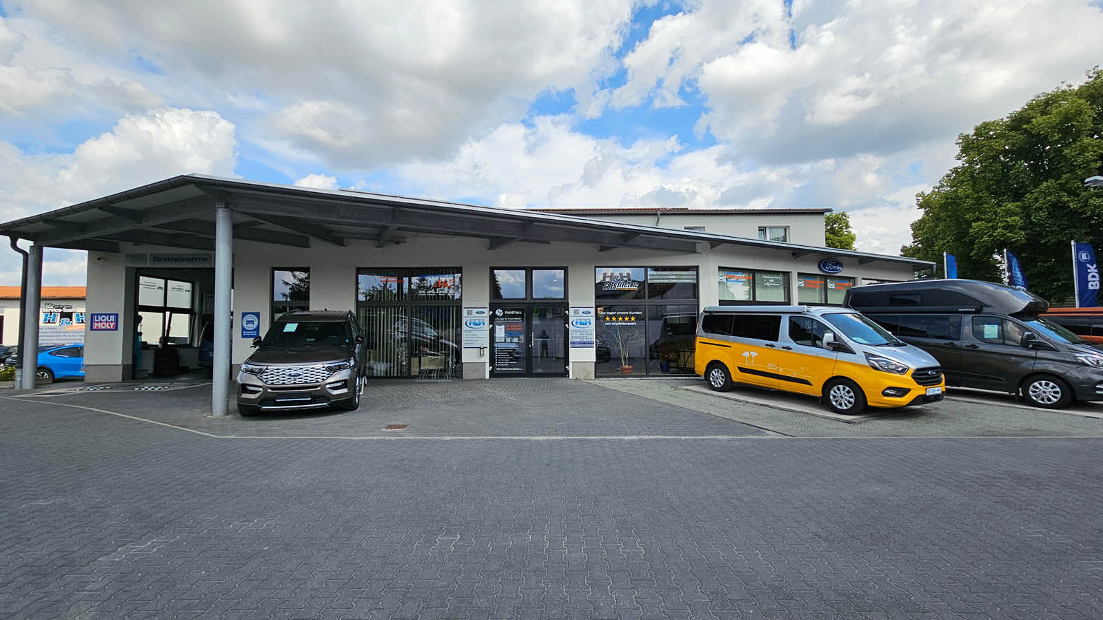 Zu sehen ist der Außenbereich von Autohaus H & H in Premnitz. Verschiedene Fahrzeuge stehen vor dem Gebäude