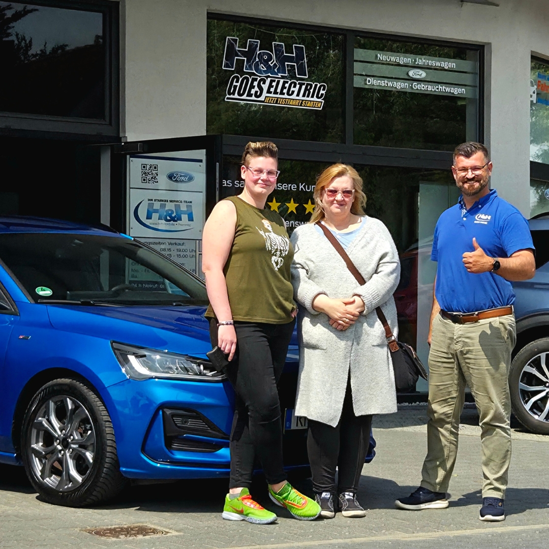 Zu sehen sind drei Personen vor dem Autohaus H&H. Im Hintergrund steht ein blaues Fahrzeug.