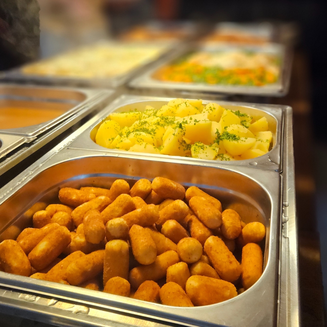 Zu sehen sind mehrere wärmebehälter eines Buffets mit Kroketten, Kartoffeln und Gemüse
