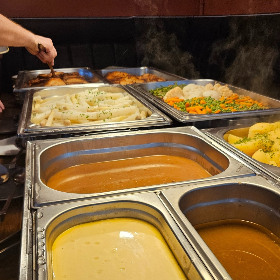 Zu sehen ist ein Ausschnitt eines warmen Buffets mit Gemüse und Soßen