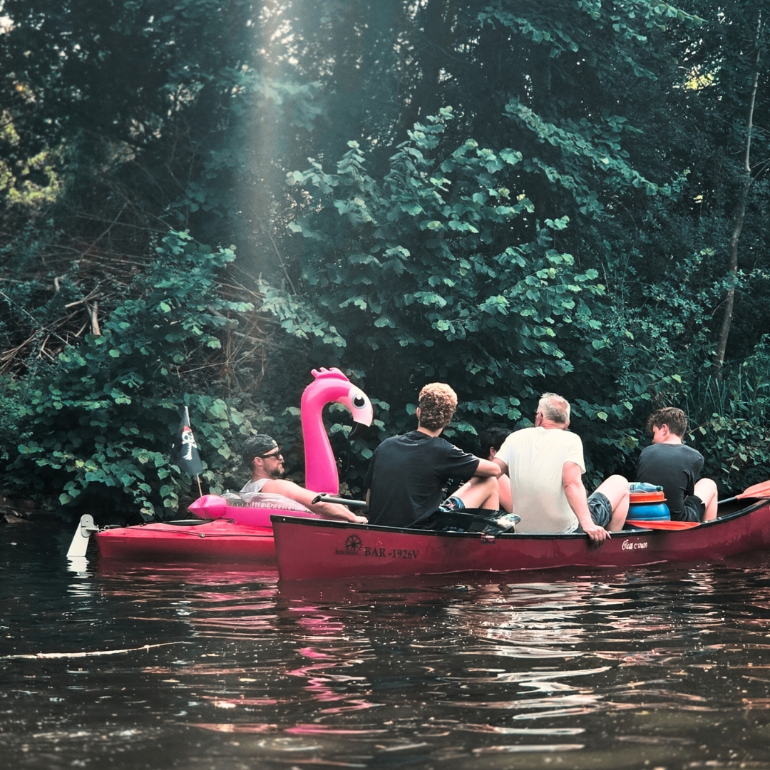Zu sehen sind mehrere Personen, die mit Kajaks über einen See fahren. Im Wasser ist auch ein  Schwimmreifen in Form eines Flamingos zu erkennen