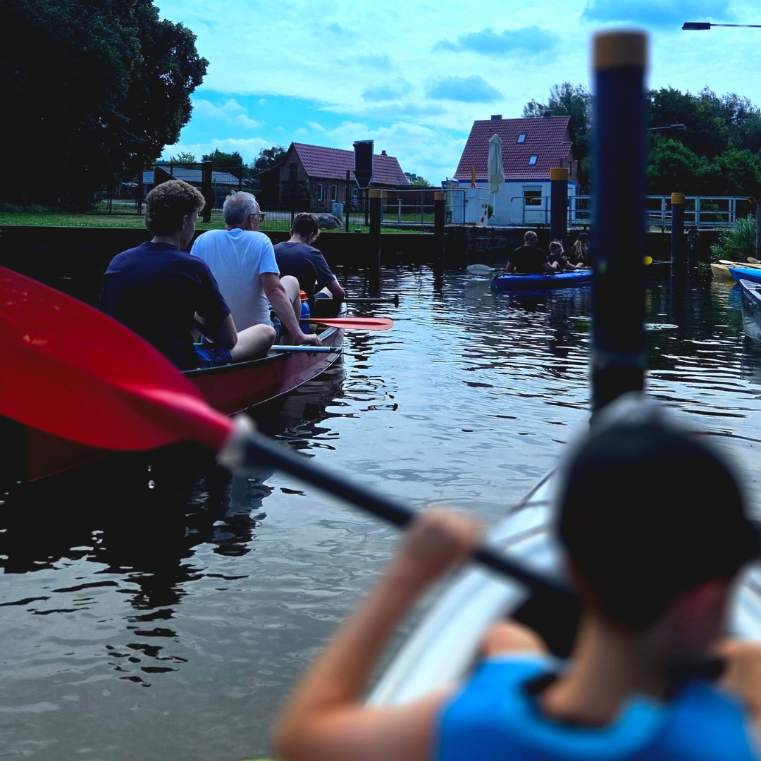 Zu sehen ist eine Gruppe von Personen, die in Kajaks auf einem See unterwegs sind.