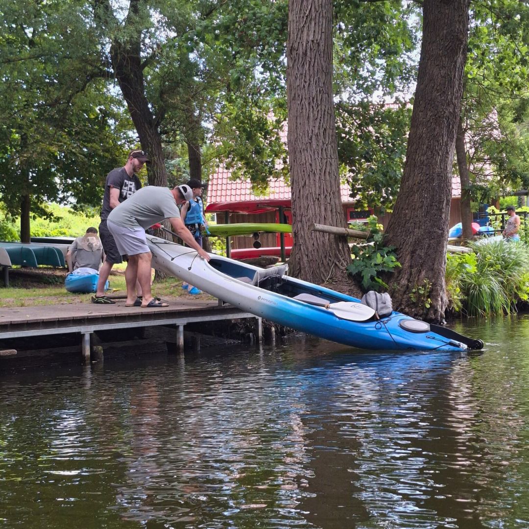 Zwei Personen sind zu erkennen, die ein Kajak vom Steg behutsam ins Wasser setzen.