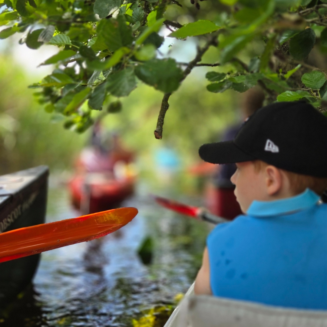 Zu sehen sind mehrere Personen, die mit Kajaks über einen See fahren.